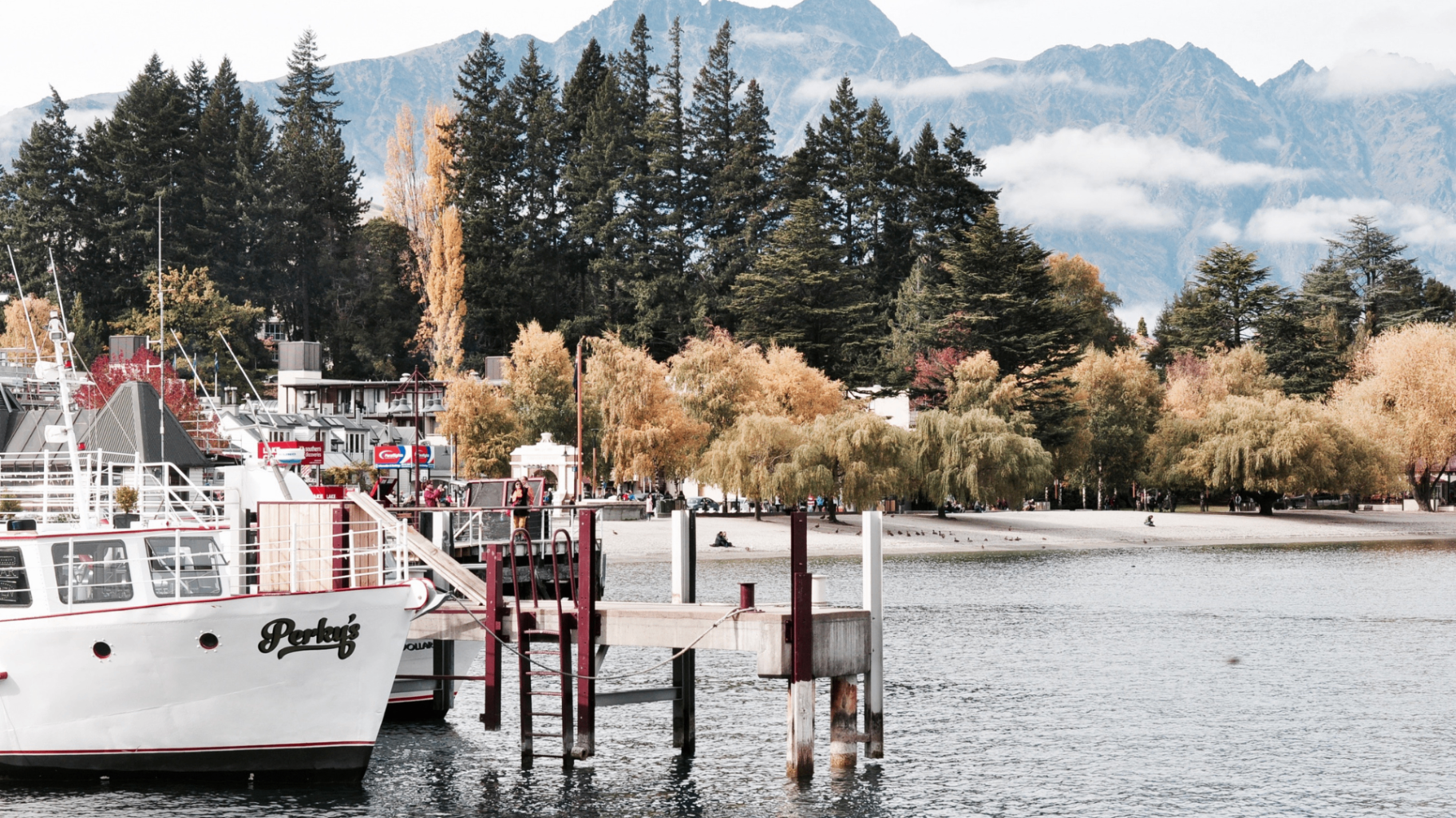 Queenstown waterfront with boats, autumn trees, and mountain backdrop