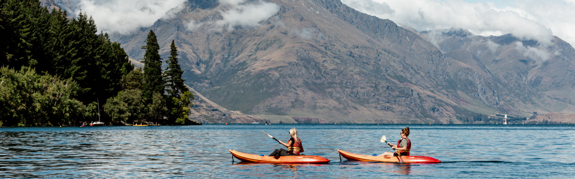 Kayakers paddling on Lake Wakatipu with mountains and clouds behind